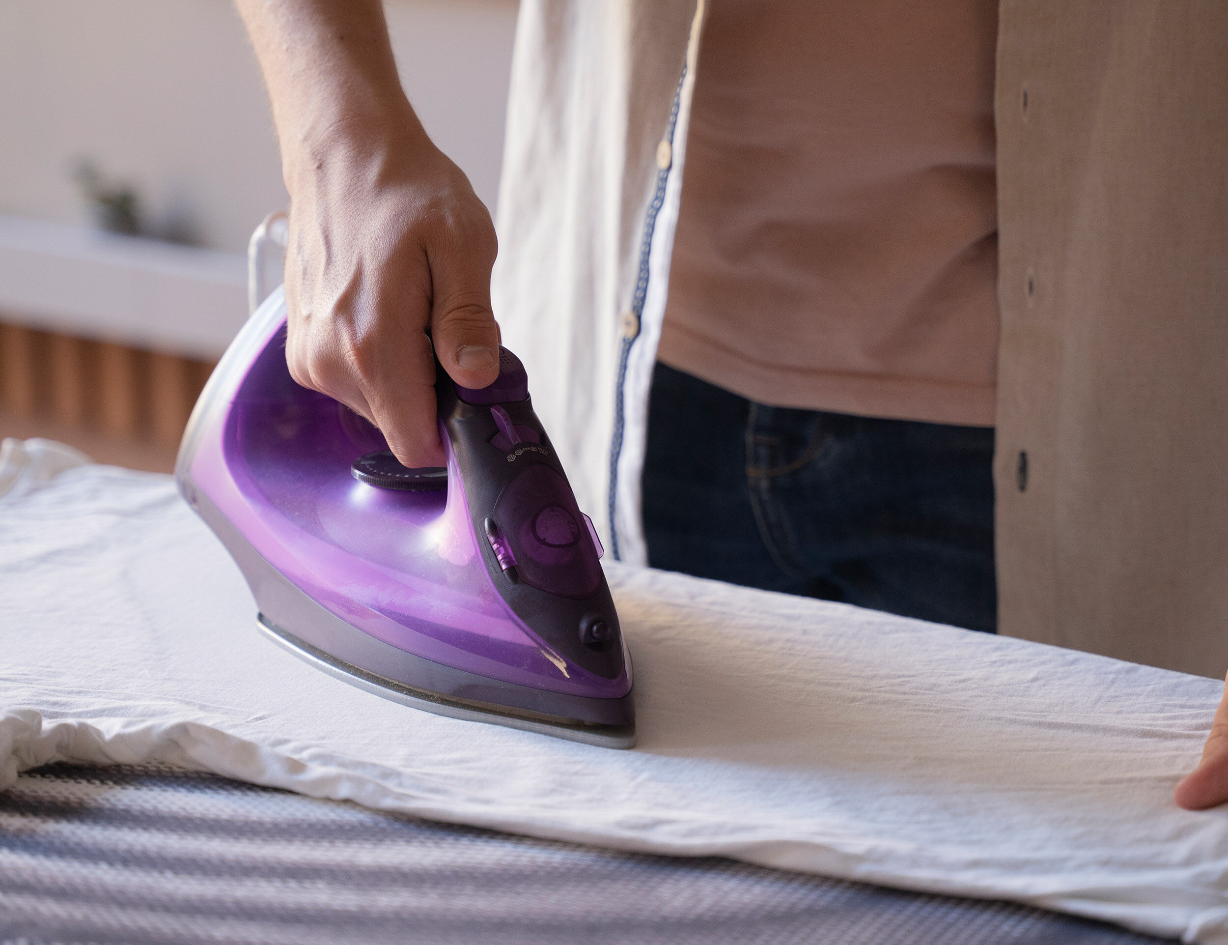Person ironing a white kurta with a purple steam iron, showing fabric care and wrinkle removal.
